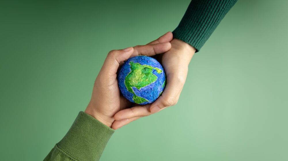 two hands holding a mini earth globe on green background