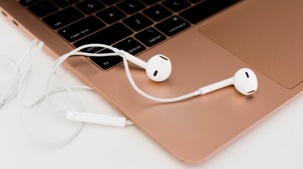 white earphones sitting on a rose gold laptop