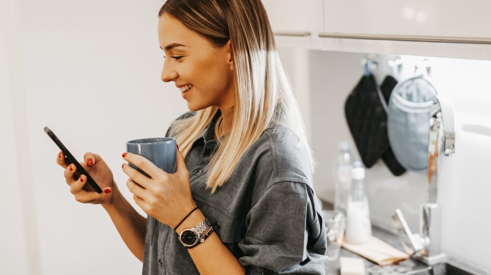 woman holding coffee cup smiling at phone