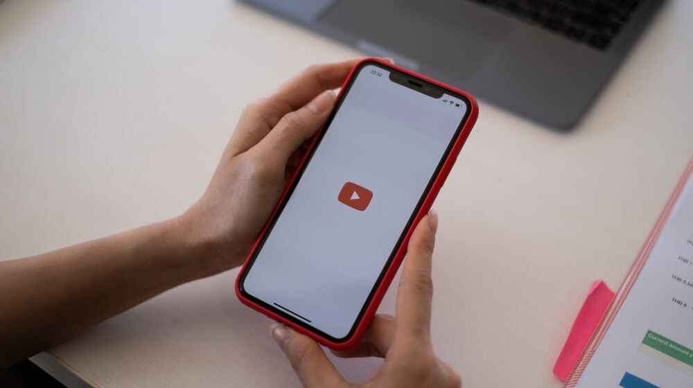 youtube logo on phone screen being held at a desk