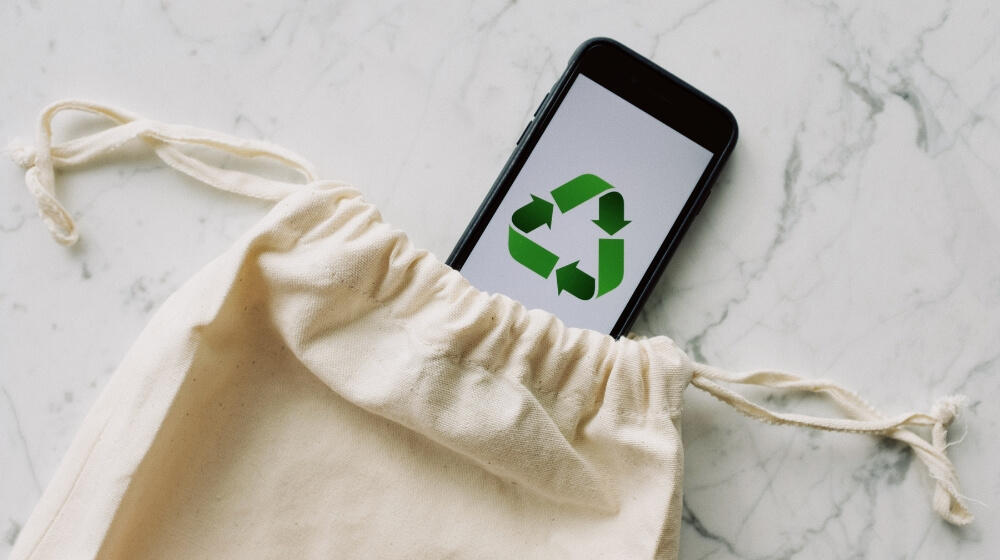 phone in white drawstring bag with a recycling symbol on screen